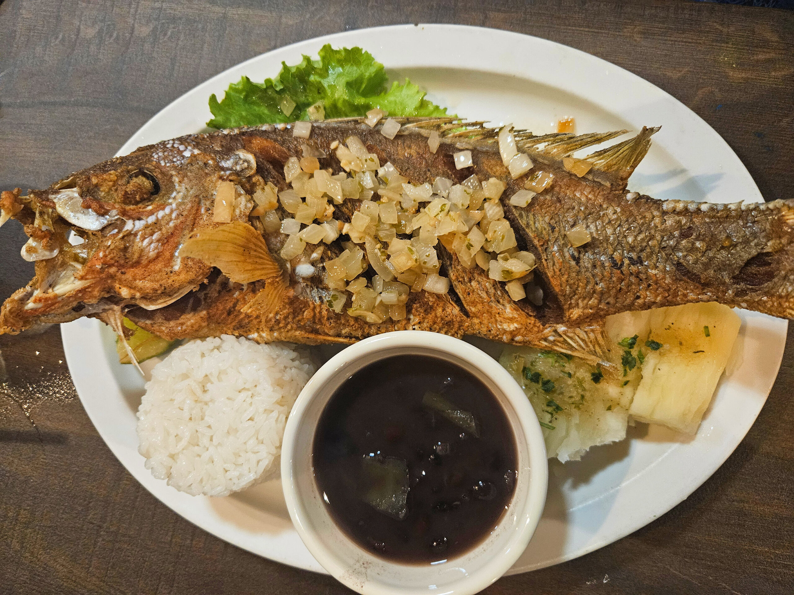 Whole fried fish topped with diced onions, served with white rice, black bean soup, lettuce, and pineapple on a white plate—an excellent choice if you’re seeking where to eat in Key West.