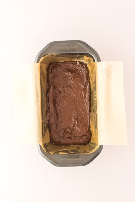 A metal loaf pan lined with parchment paper is filled with unbaked batter, ready to go into the oven.