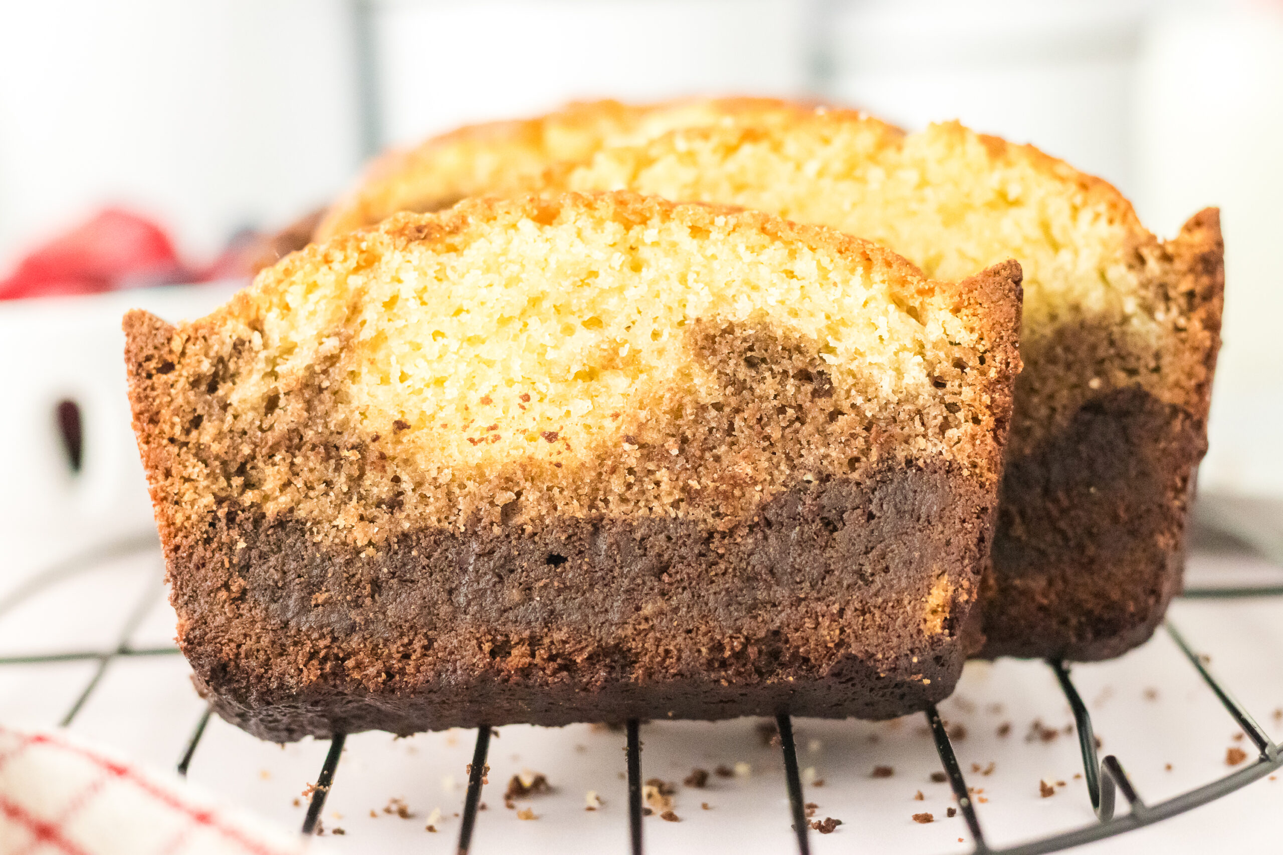Two slices of Chocolate Ombre Pound Cake with distinct chocolate and vanilla layers rest on a cooling rack, showing a moist texture and golden brown crust.