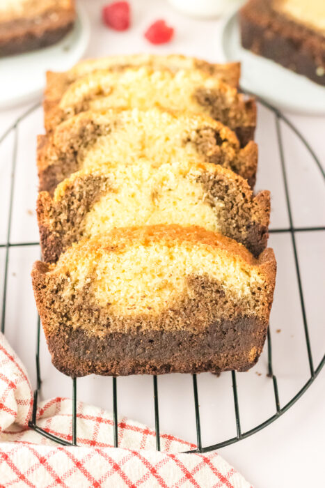 Four slices of Chocolate Ombre Pound Cake, featuring chocolate and vanilla swirls, are arranged on a round wire cooling rack, with a red and white towel in the foreground.
