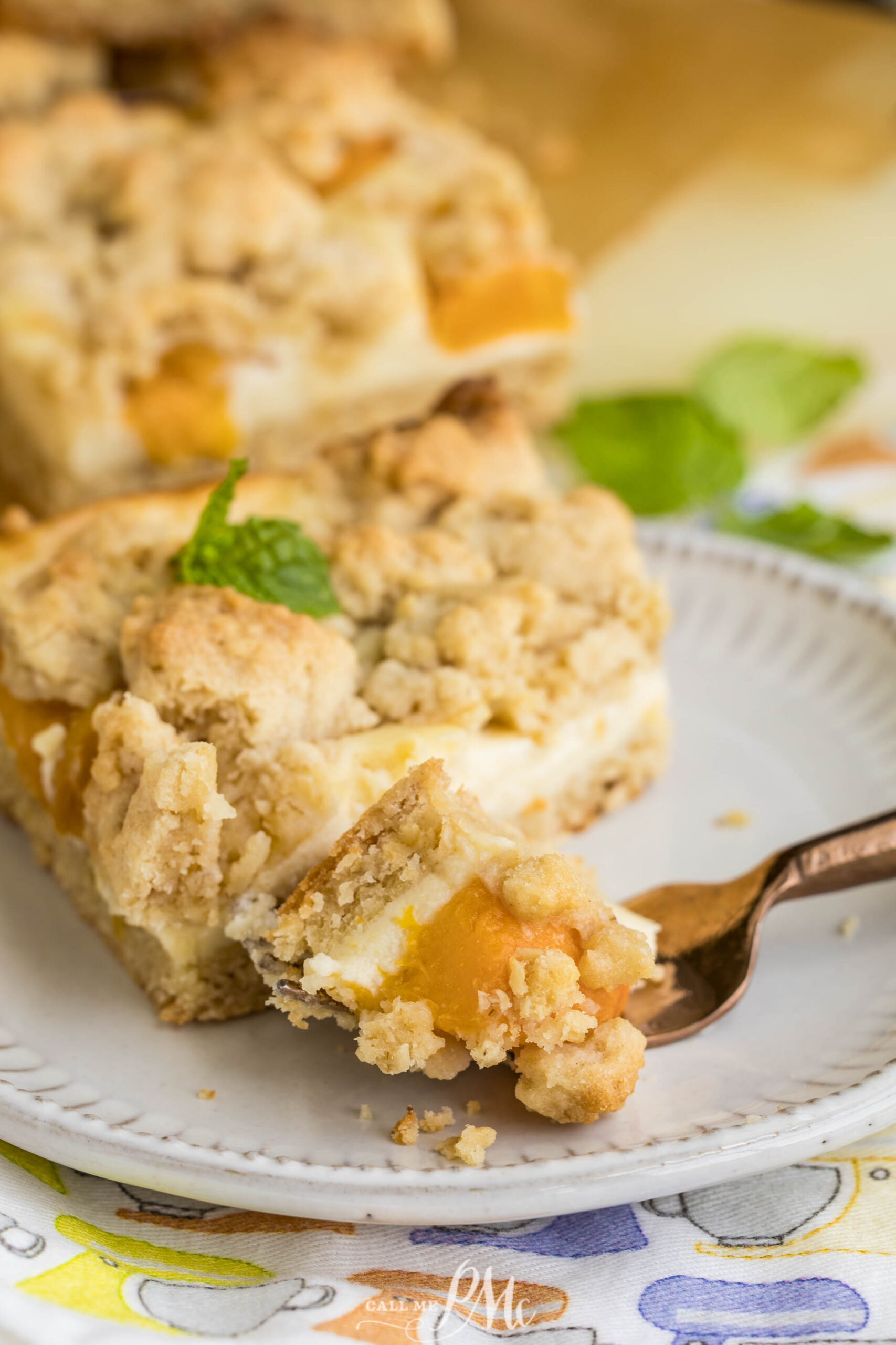 A close-up of a fork holding a bite of Peach Cheesecake Crumb Bars with a crumbly topping, creamy filling, and juicy peach pieces, on a white plate.