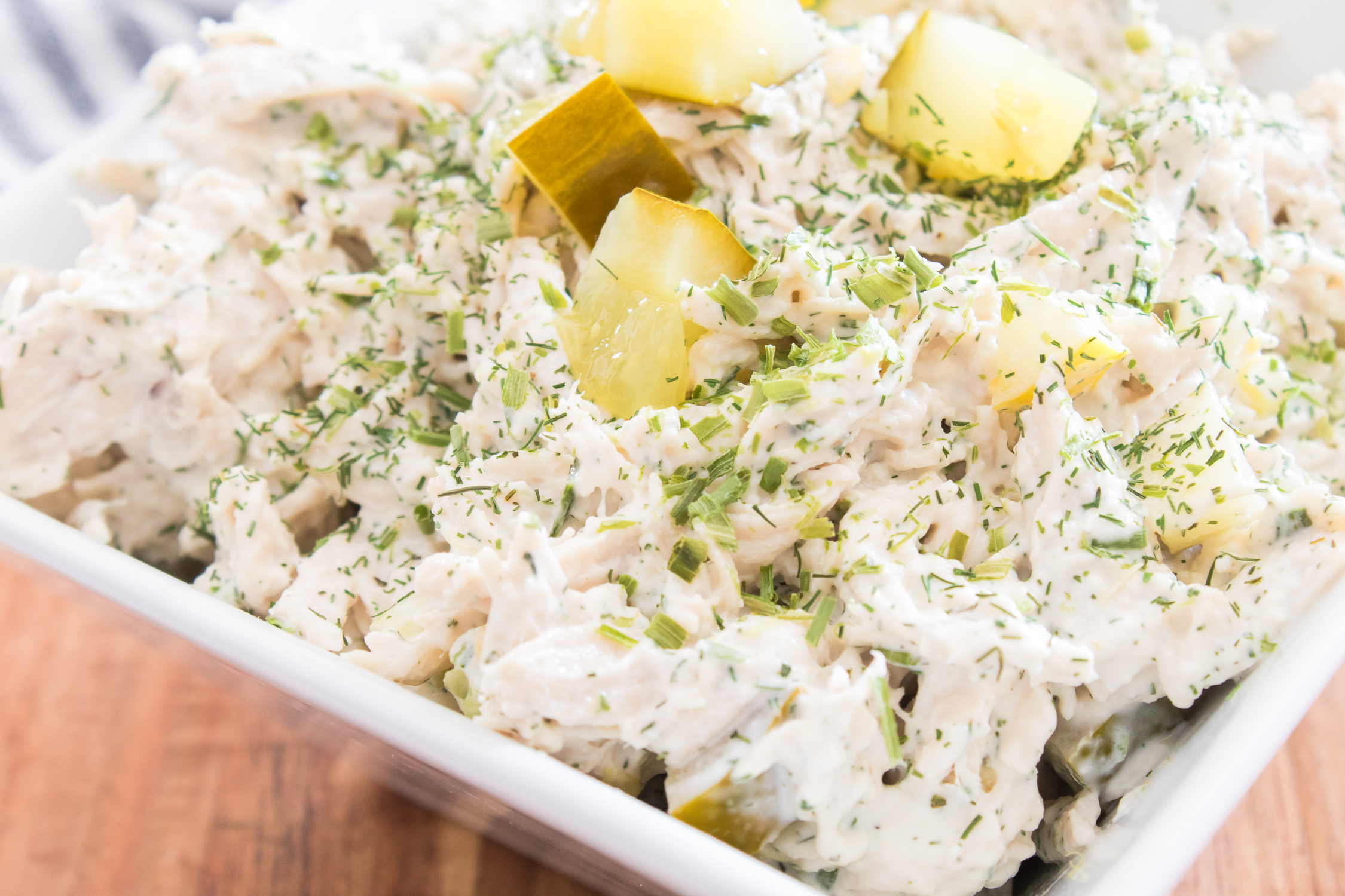 Dill pickle chicken salad with creamy dressing, chopped pickles, and sprinkled herbs, served in a white bowl on a wooden surface.