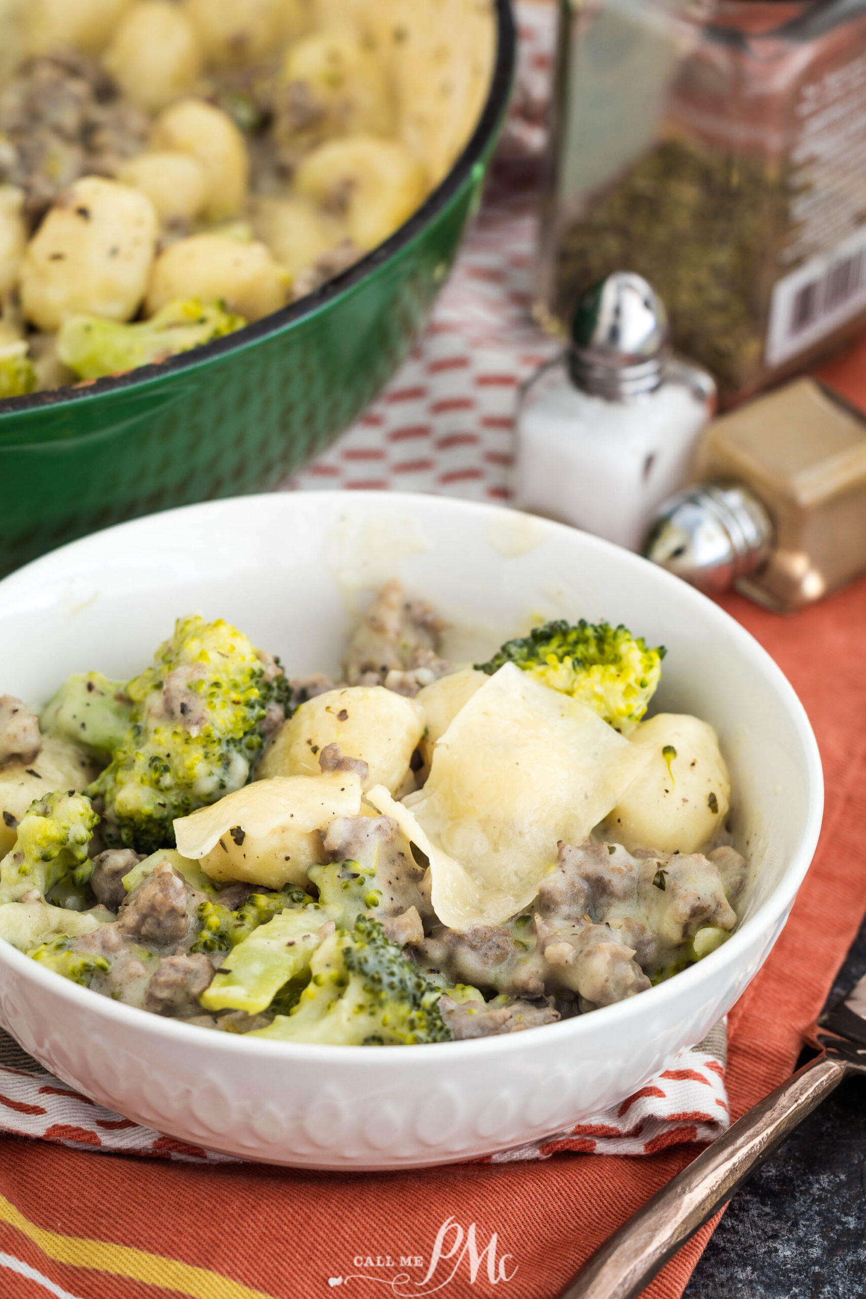 A white bowl filled with dinner. A pot with more food and seasoning containers are in the background.