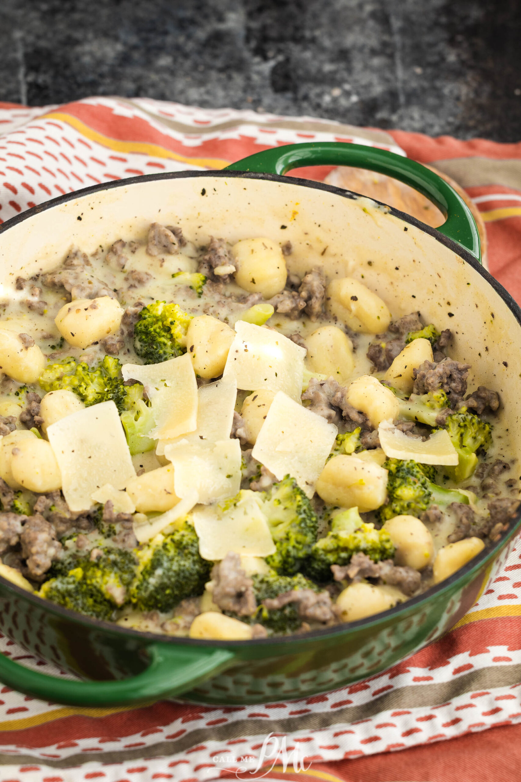 Green Dutch oven filled with food, sitting on a multi-colored cloth.