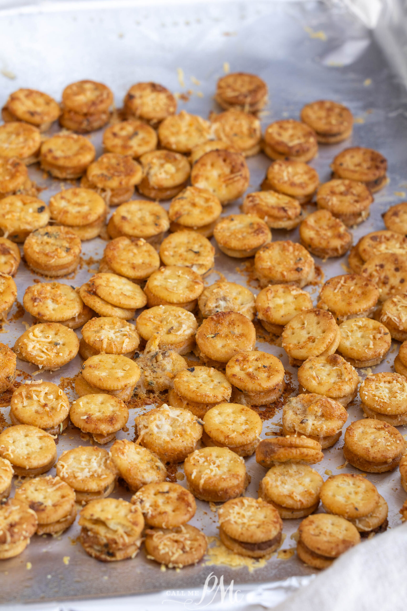 A baking sheet covered with many golden-brown garlic bread Ritz Bits cracker sandwiches topped with grated cheese.
