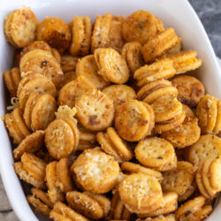 A white bowl filled with garlic bread Ritz Bits sandwiches topped with grated cheese.