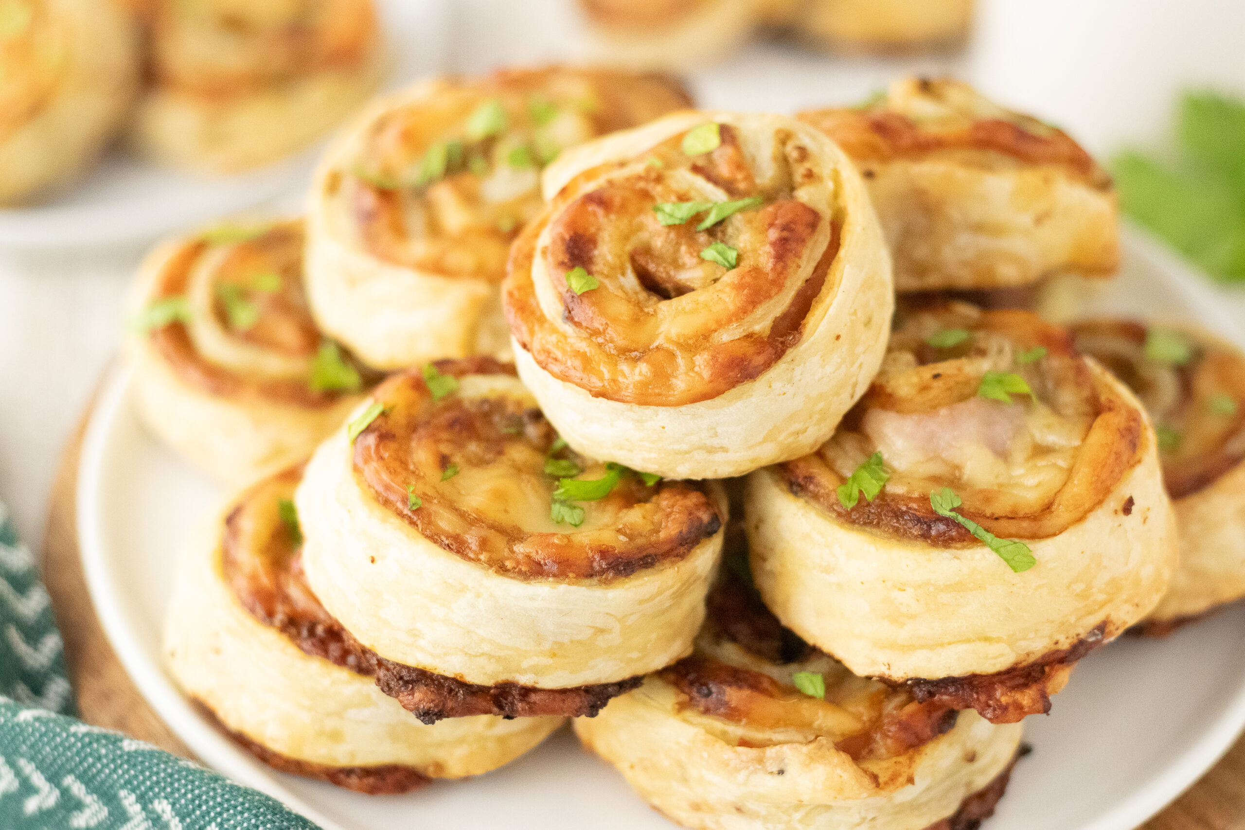 A stack of golden brown ham and cheese pinwheels topped with fresh herbs on a white plate.