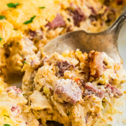 A spoonful of Reuben casserole dip containing corned beef, Swiss cheese, and sauerkraut being lifted from a baking dish.