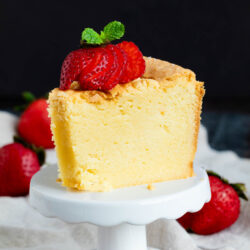 A slice of yellow white chocolate pound cake topped with sliced strawberries and mint, served on a small white pedestal stand.