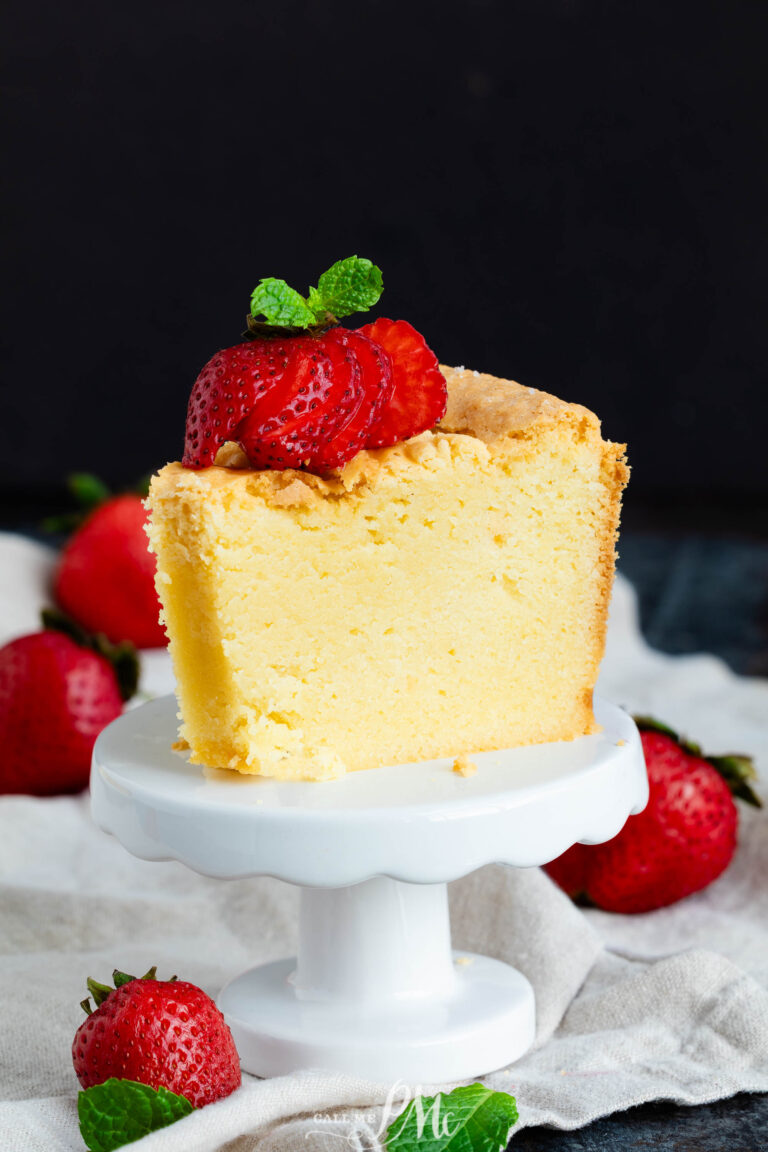 A slice of yellow white chocolate pound cake topped with sliced strawberries and mint, served on a small white pedestal stand.
